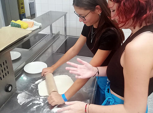 Zwei Schülerinnen beim Pizzateig ausrollen