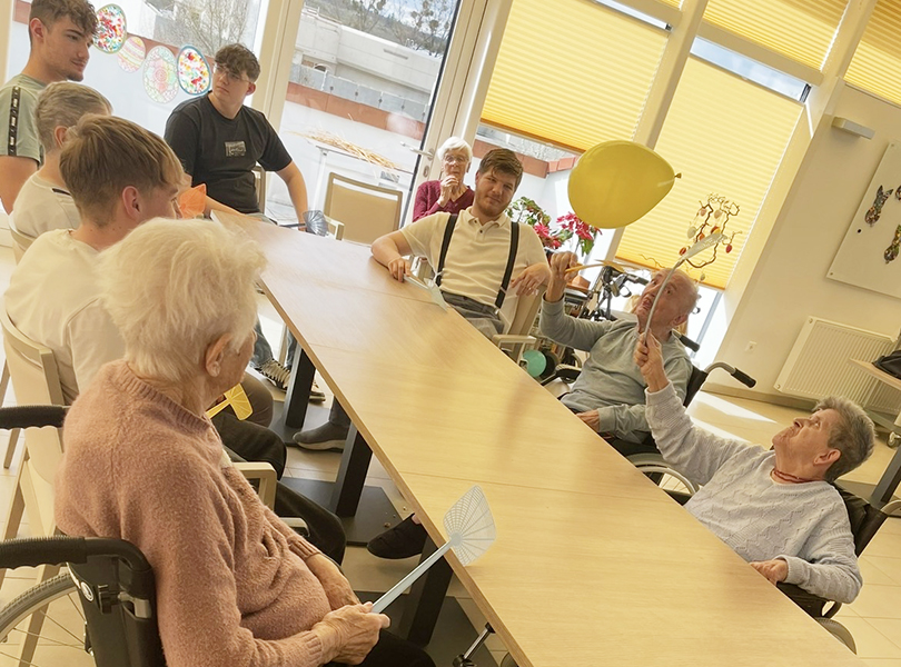 Schüler mit Bewohner des Altenwohnheims spielen mit Luftballon