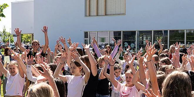 Schülerinnen und Schüler strecken bei einer Aktion im Freien die Hände in die Höhe
