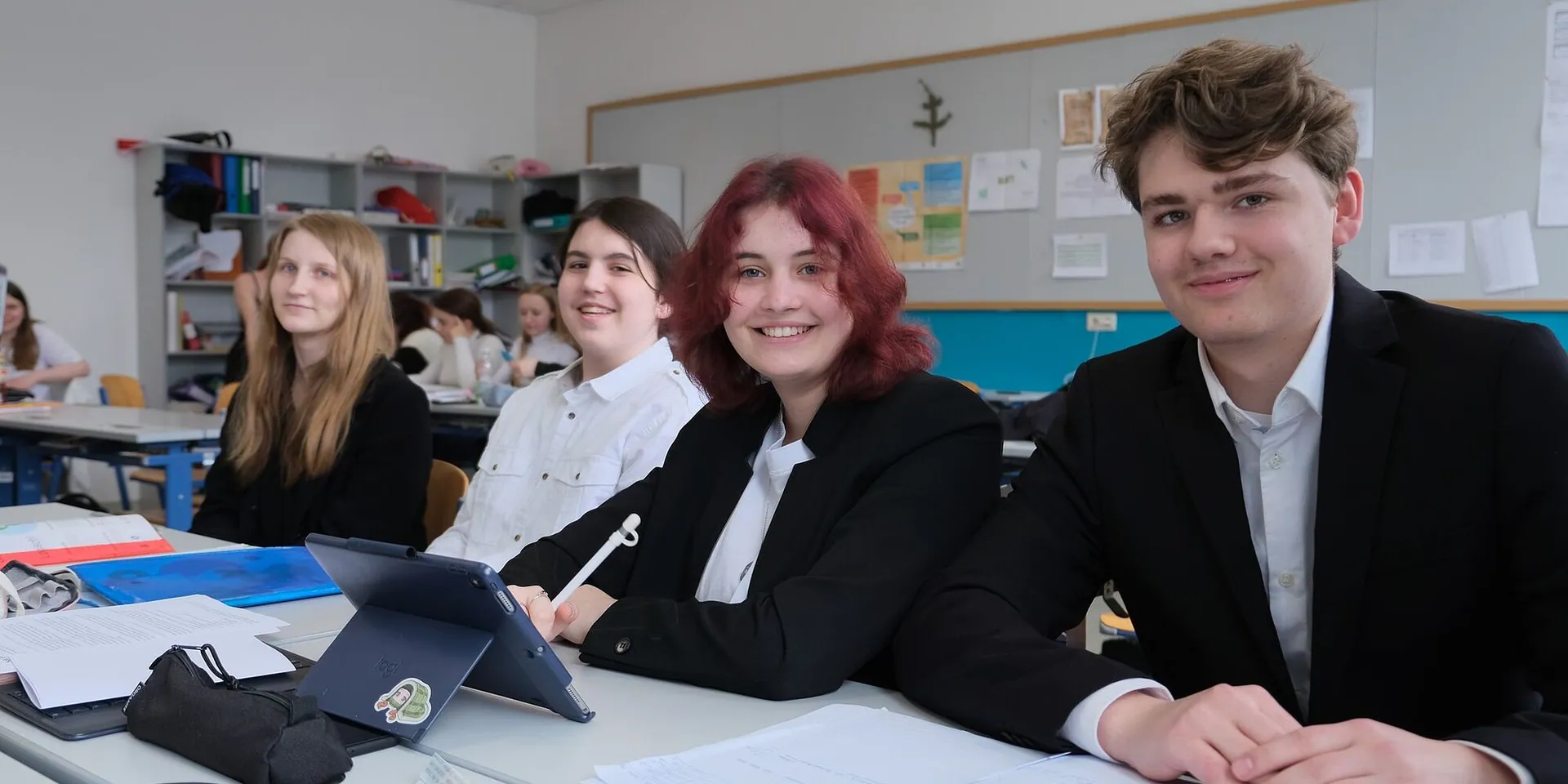 Schülerinnen und Schüler im Business-Outfit lächeln beim Business Day in die Kamera
