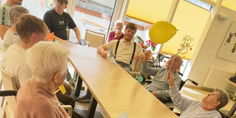 Schülerinnen und Schüler spielen mit einer Bewohnerin des Altenwohnheims mit einem Luftballon