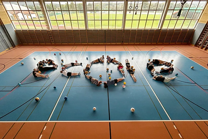 Schülerinnen und Schüler bilden im Turnsaal liegend das Wort ecole