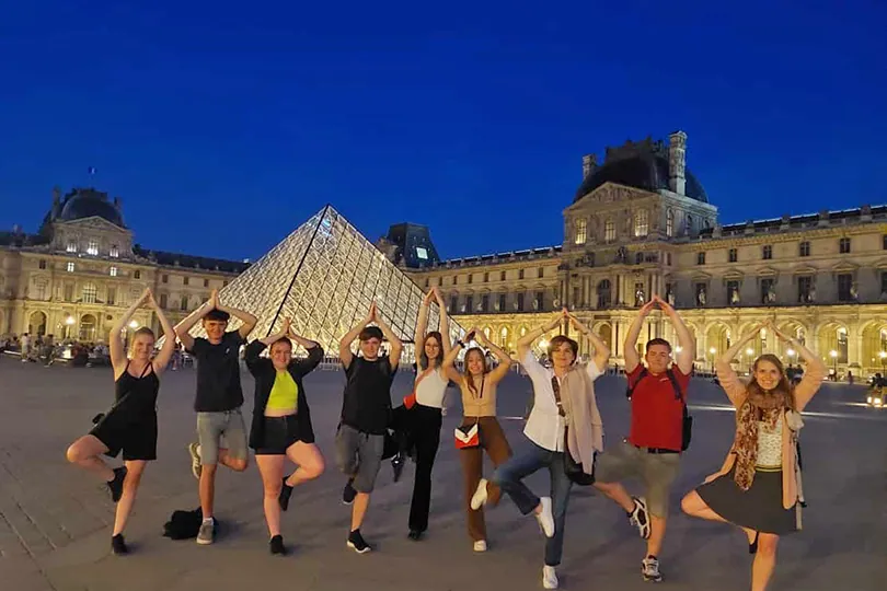 Schülerinnen und Schüler springen vor der Pyramide des Louvre in die Luft